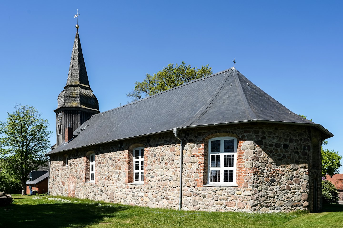 Historyczny kamienny kościół z drewnianą wieżą stoi na trawie.
